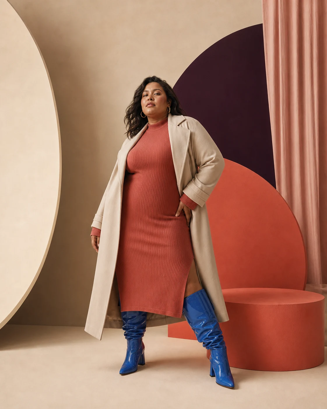 Modella plus-size con abito corallo, cappotto chiaro e stivali blu