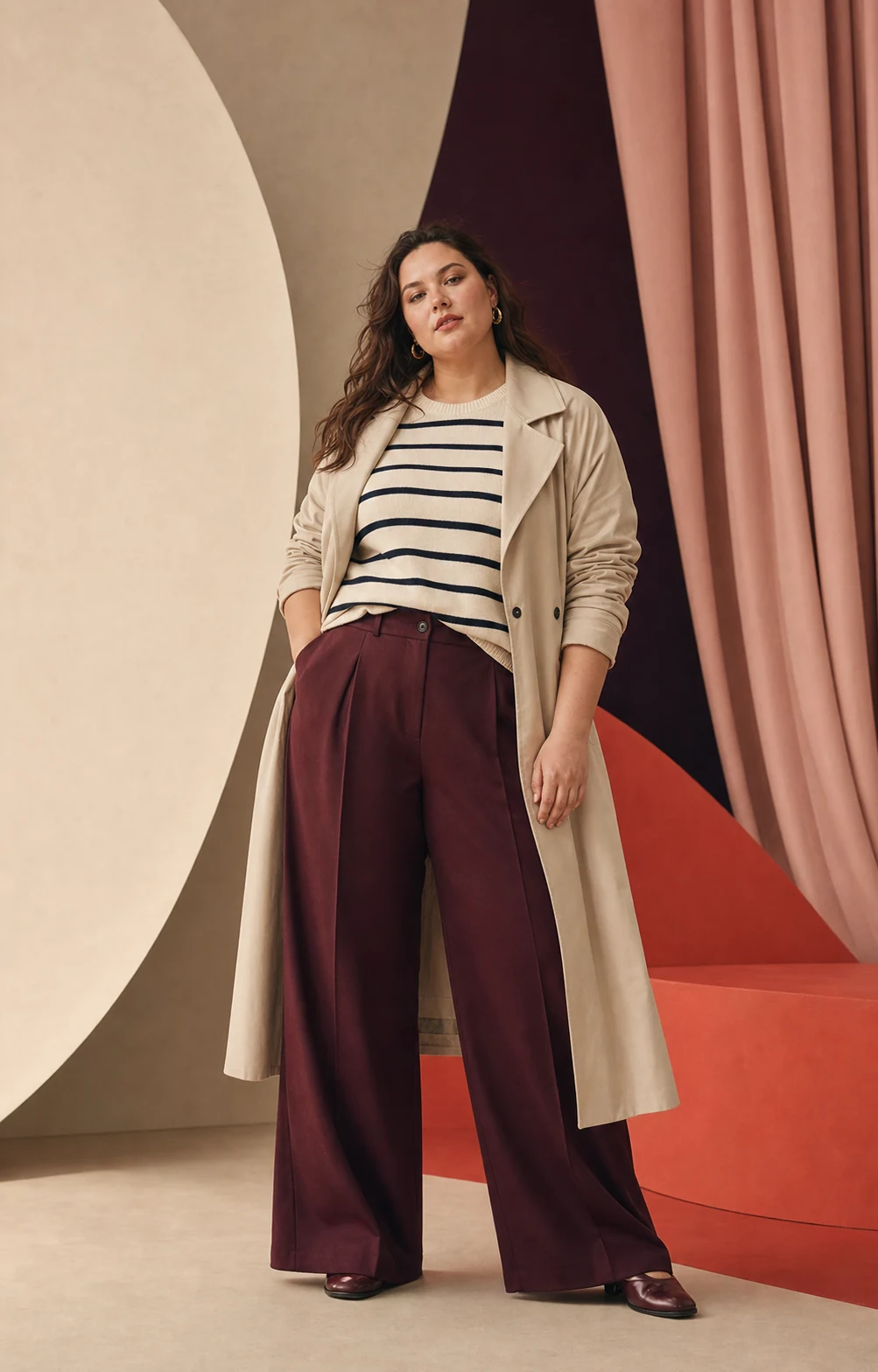 Modella plus-size con trench chiaro, maglia a righe e pantaloni bordeaux