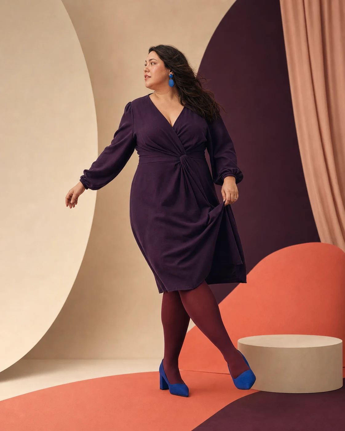Modella plus-size con abito prugna, collant colorati e scarpe blu
