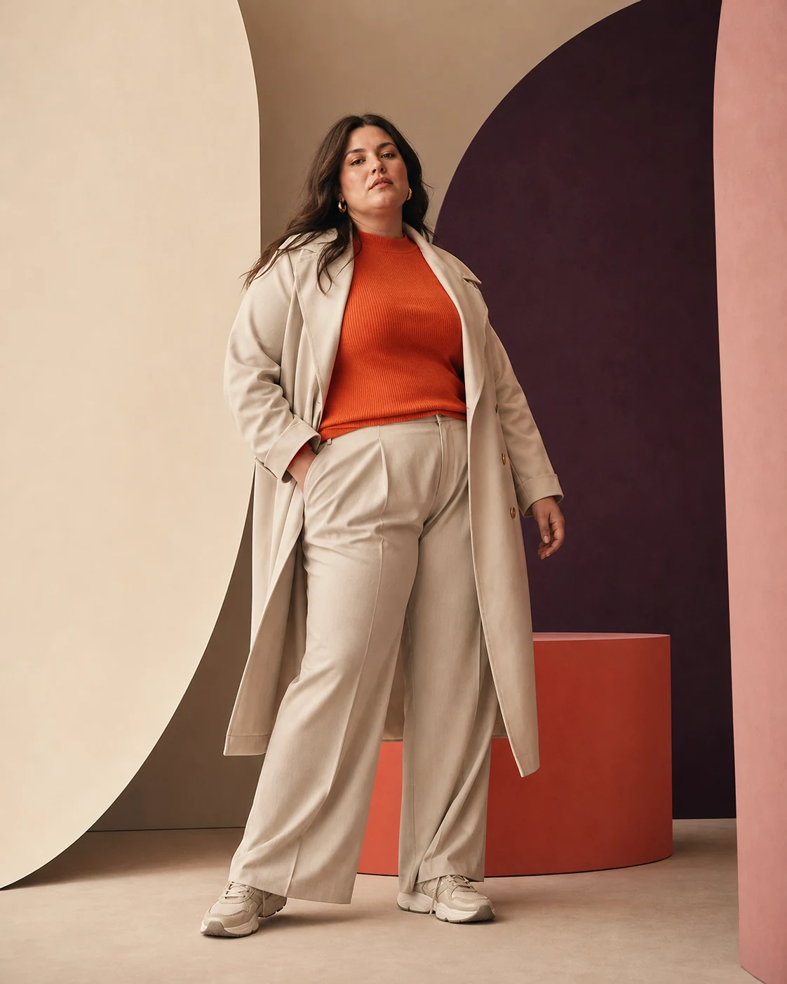 Modella plus-size con cappotto chiaro, top corallo e pantaloni fluidi
